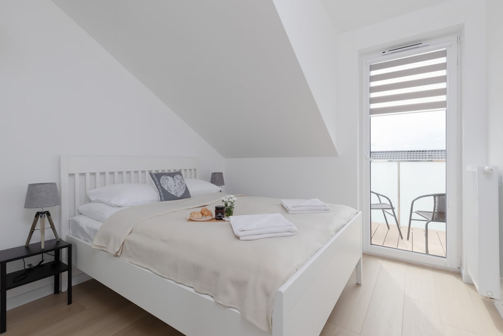 A minimalist bedroom with white bedding, a slanted ceiling, and a serene, clean design.