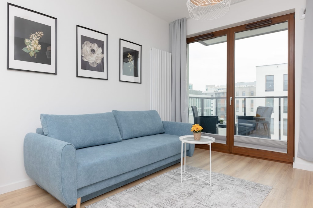 A cozy living room featuring a blue sofa, a coffee table, and a balcony view.
