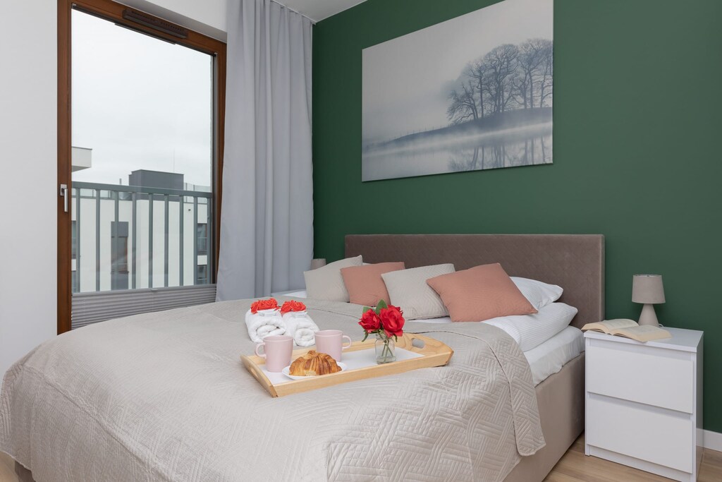 A bedroom with a large bed, green accent wall, and bedside tables.
