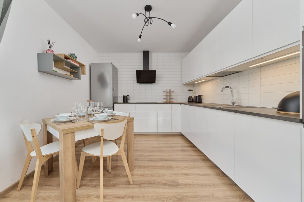 A dining area and kitchen with wooden furniture, sleek white cabinetry, and modern lighting.

