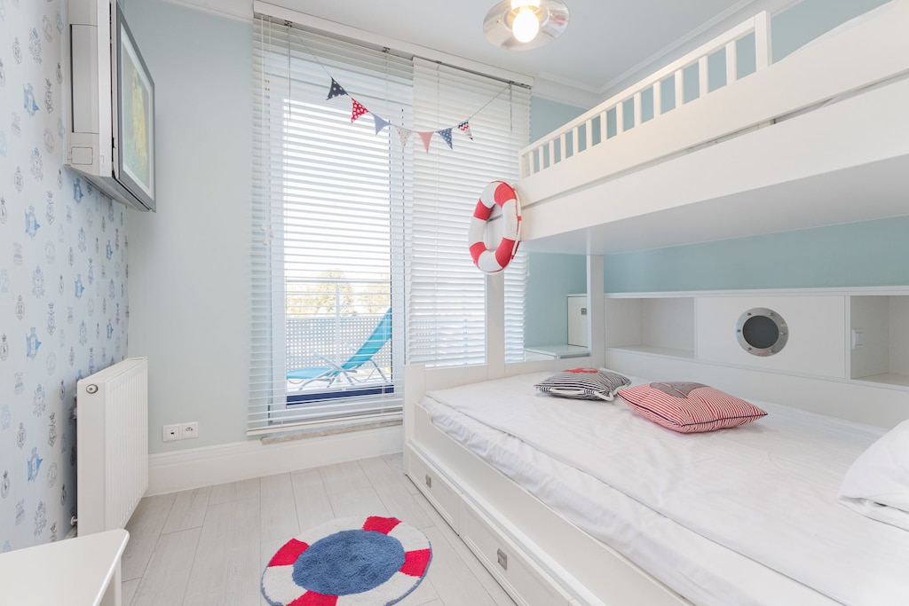 A charming children’s bedroom with white bunk beds, nautical-themed bedding, and decorative life buoys on the walls.