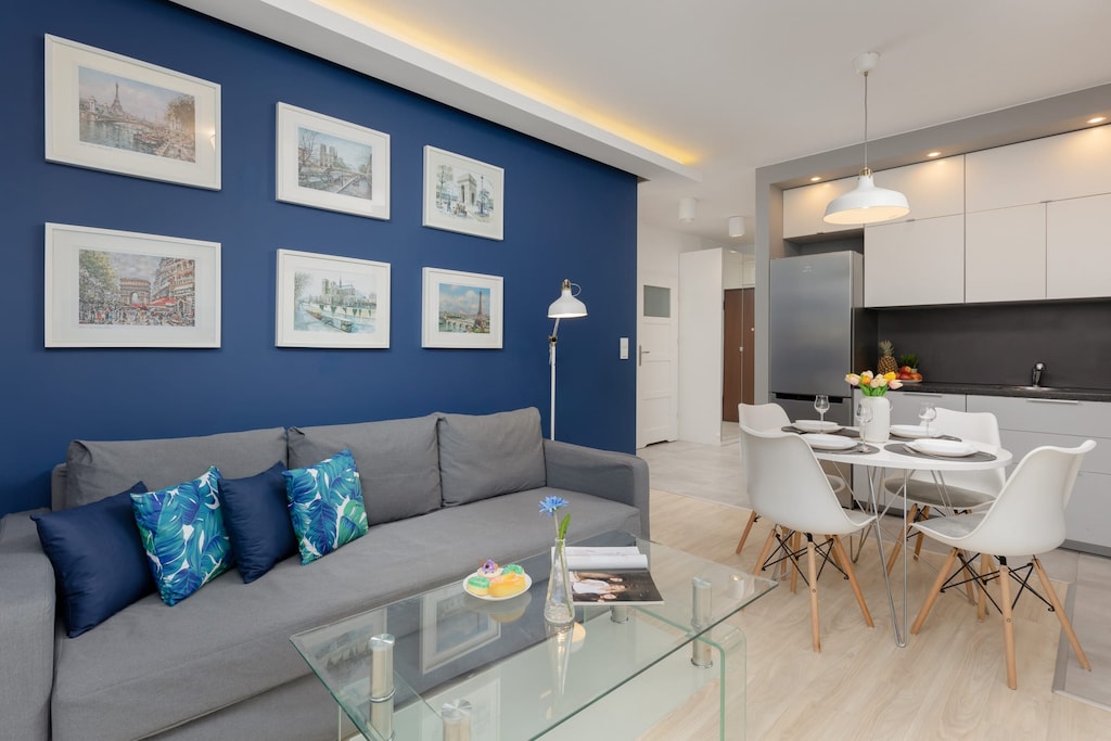 A stylish living room featuring a blue accent wall, a comfortable sofa, and a glass coffee table, adjacent to a dining area.