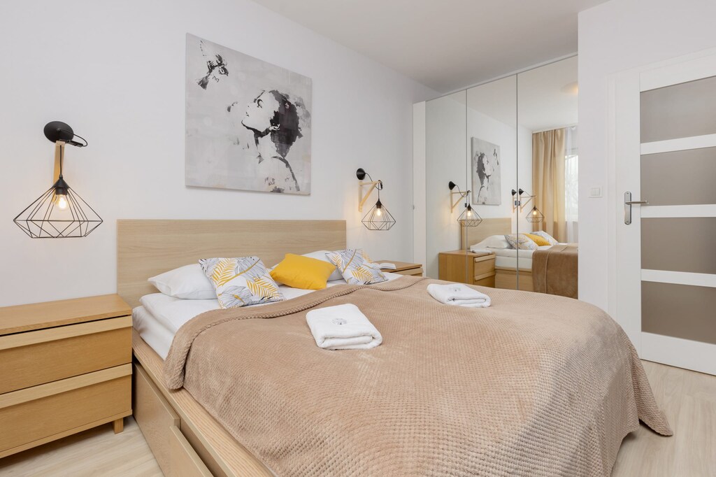 A cozy bedroom with a bed covered in beige bedding, wooden furniture, and soft lighting.