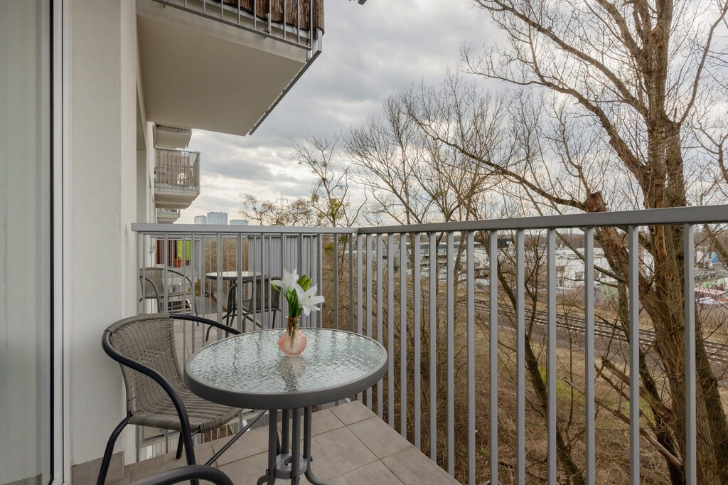 A balcony featuring a small round table and chairs, overlooking a scenic outdoor area with trees.