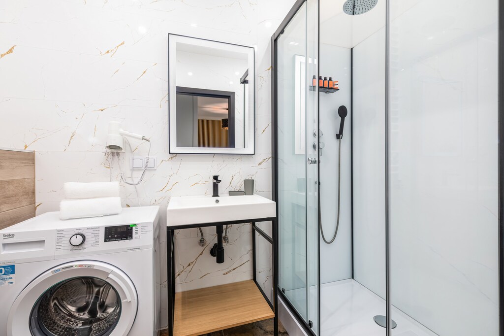 A compact bathroom with a walk-in shower, washing machine, and wooden elements, blending practicality with a modern design.

