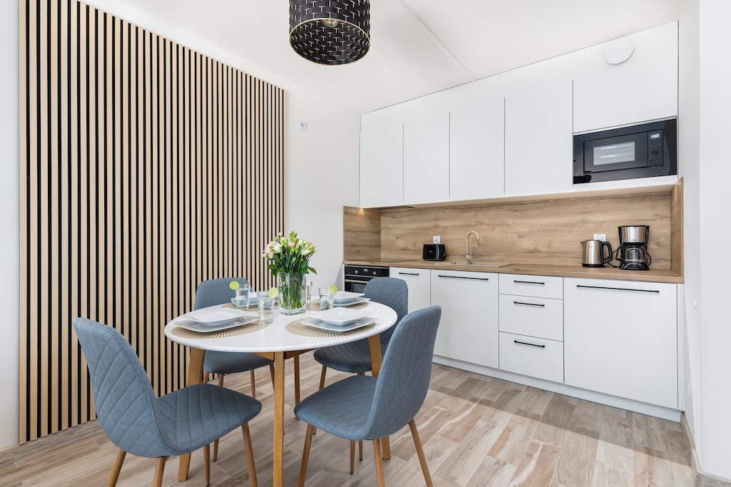 A sleek open-plan kitchen and dining area with wooden accents, a round dining table, and modern appliances for a functional yet elegant space.

