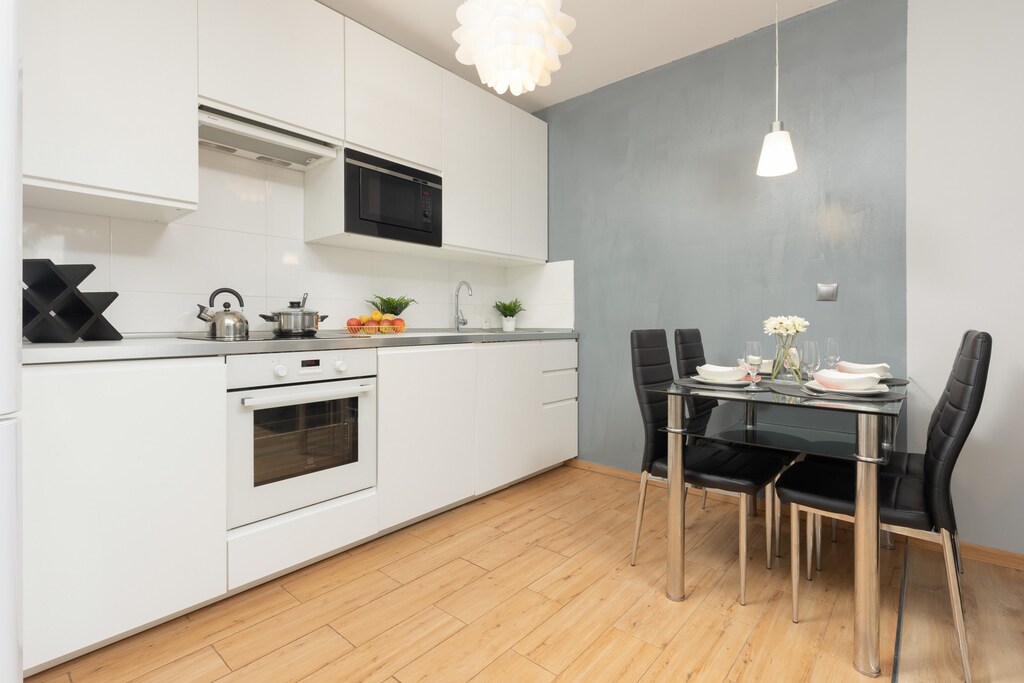 A modern kitchen with white cabinets, a dining table, and pendant lighting.
