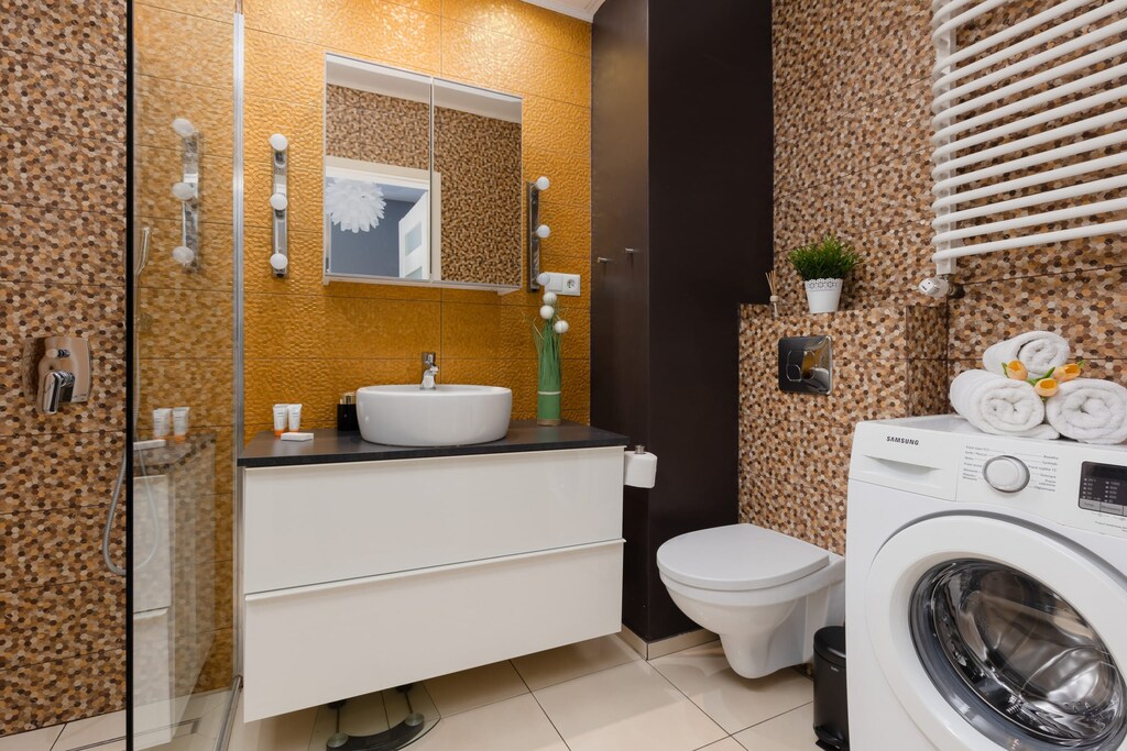 A stylish bathroom with gold and white accents, including a washing machine and a large vanity mirror.
