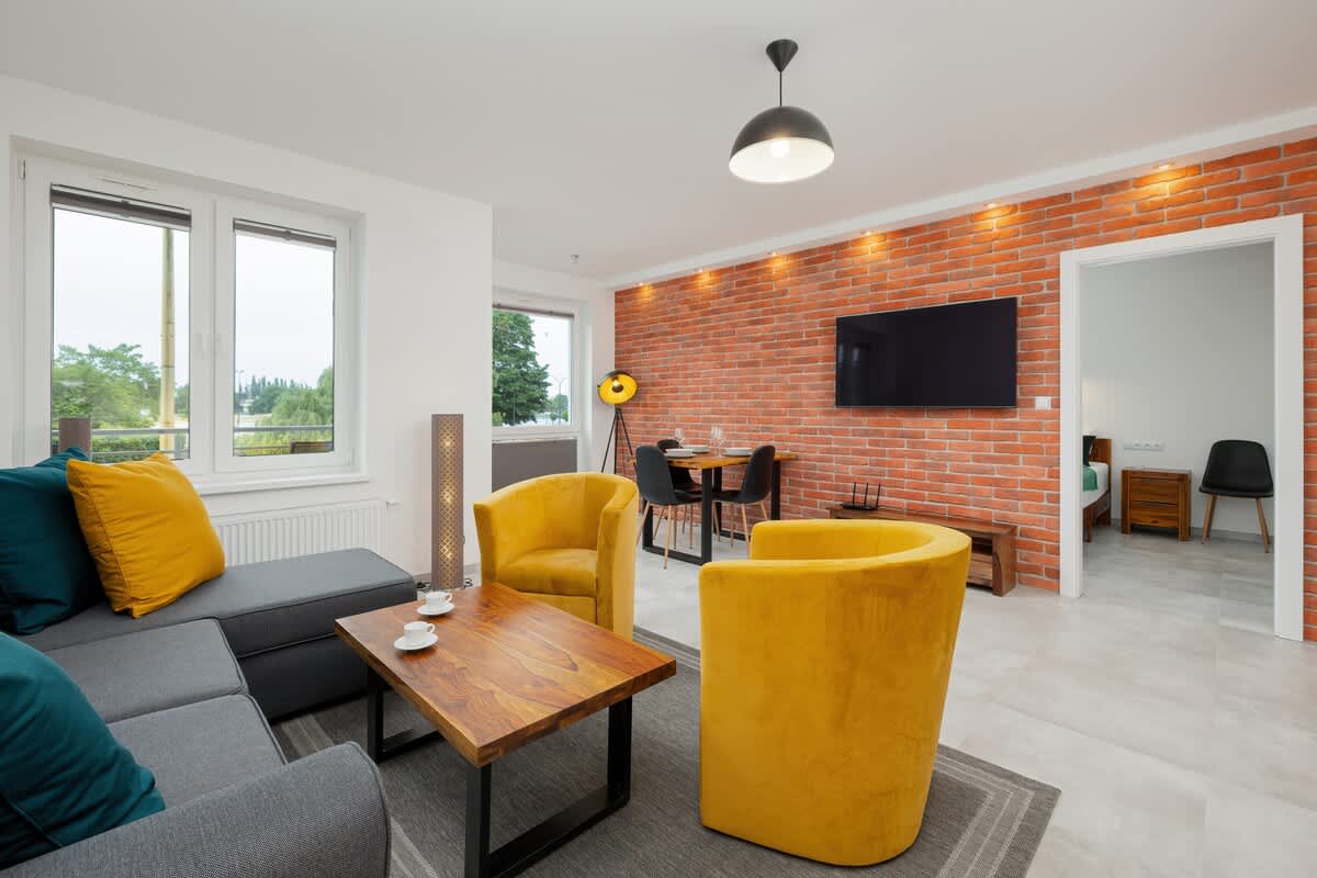 Bright, stylish loft-style living room with a brick wall with a large TV, yellow armchairs and a grey sofa.