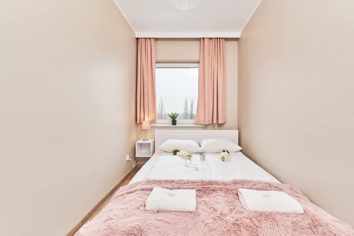 A soft pink-themed bedroom with a large bed, fresh bedding, and flowers placed decoratively on the pillow.