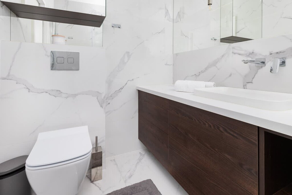 A stylish bathroom with marble tiles, a dark wooden vanity, and a modern walk-in shower.
