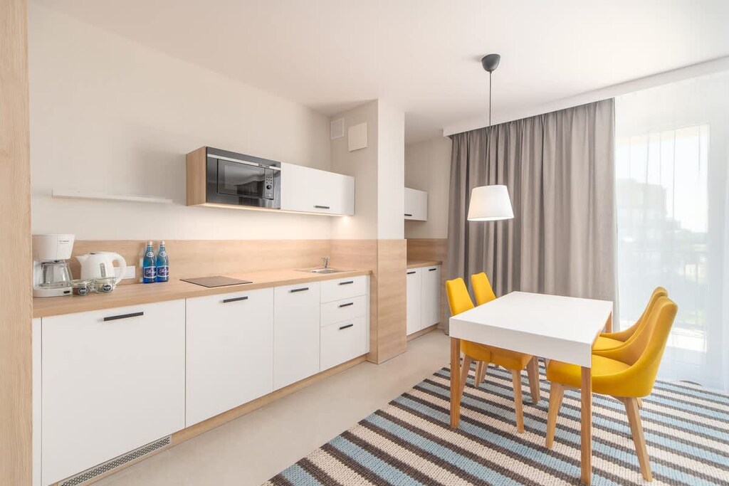 An open-plan kitchen and dining area with white cabinets, wooden countertops, and yellow chairs, blending practicality with a modern design.
