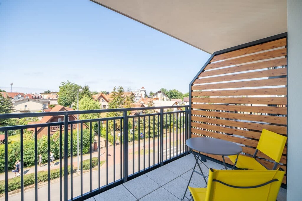 A balcony with a small table and chairs, wooden privacy panels, and a view of the surrounding residential area.
