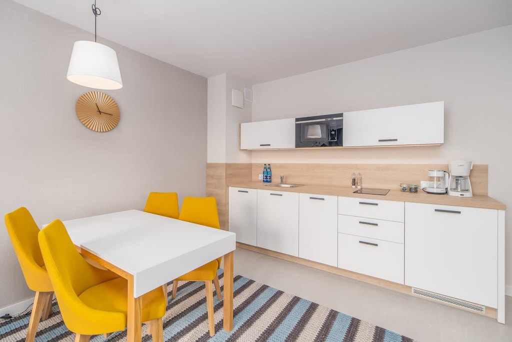 A compact kitchen and dining area with white cabinets, wooden accents, and yellow chairs, blending style and functionality.
