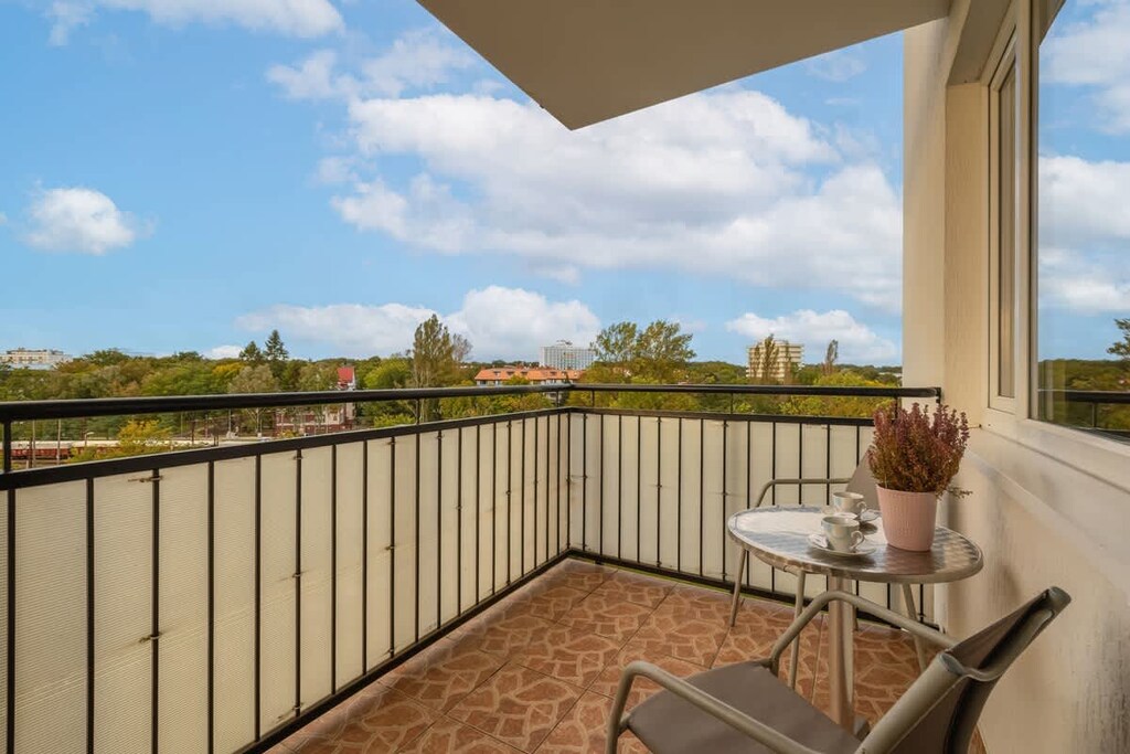 A balcony with a small table and chairs, offering a relaxing view of the greenery outside.
