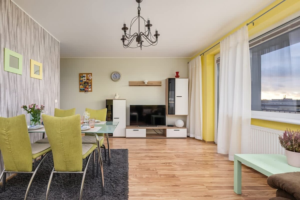 Another angle of the living-dining area, showcasing a chandelier, large windows, and decorative accents.
