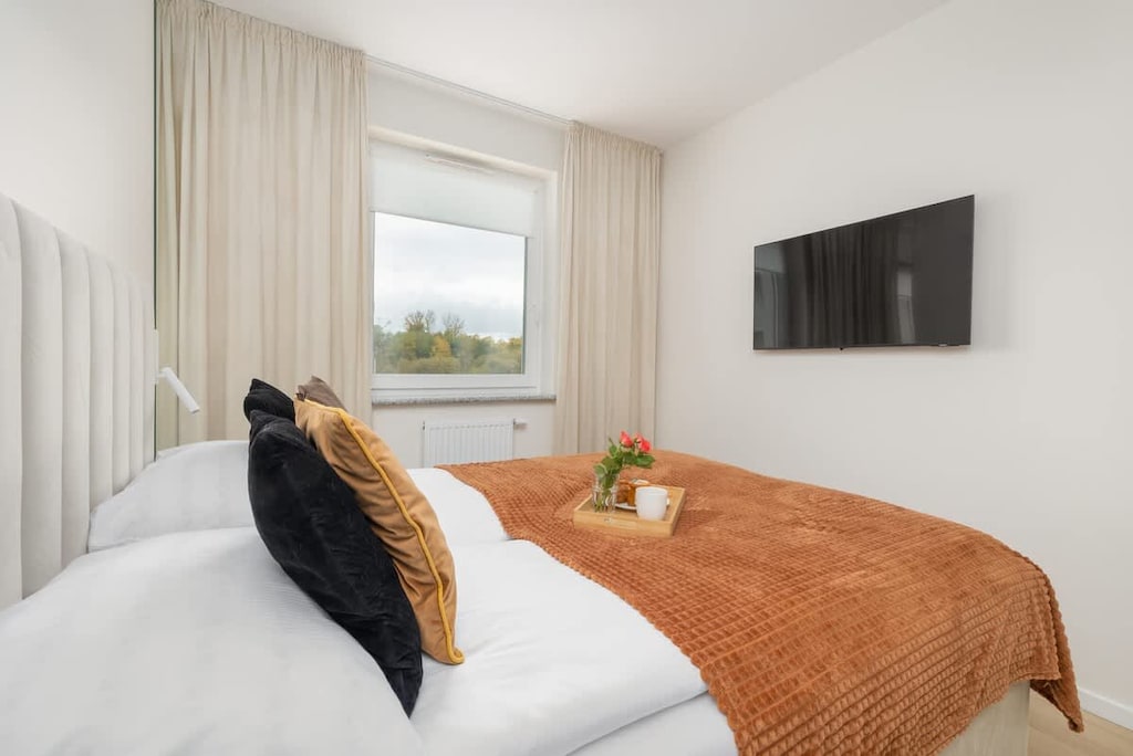 A cozy bedroom with a neatly made bed, warm-toned bedding, and a TV mounted on the wall.
