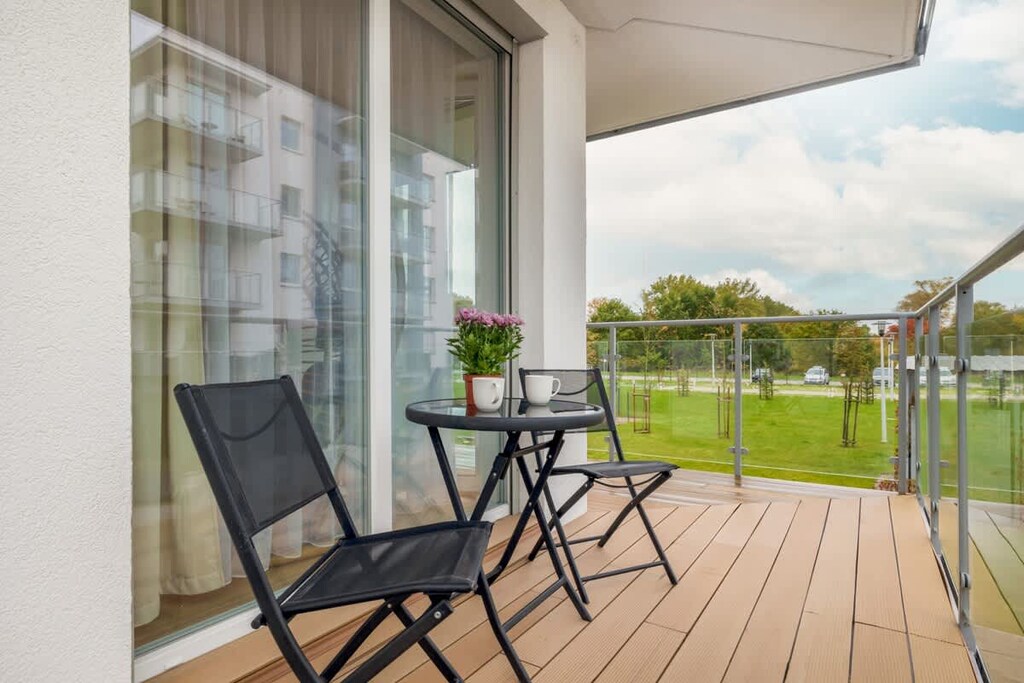 A spacious balcony with two black chairs and a small table, overlooking a green landscape.
