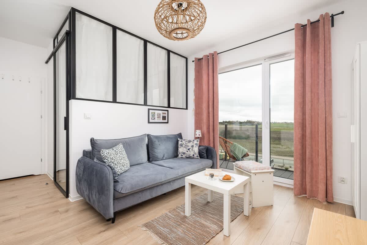 Another angle of the living room, showcasing the large window, gray sofa, and cozy furnishings.

