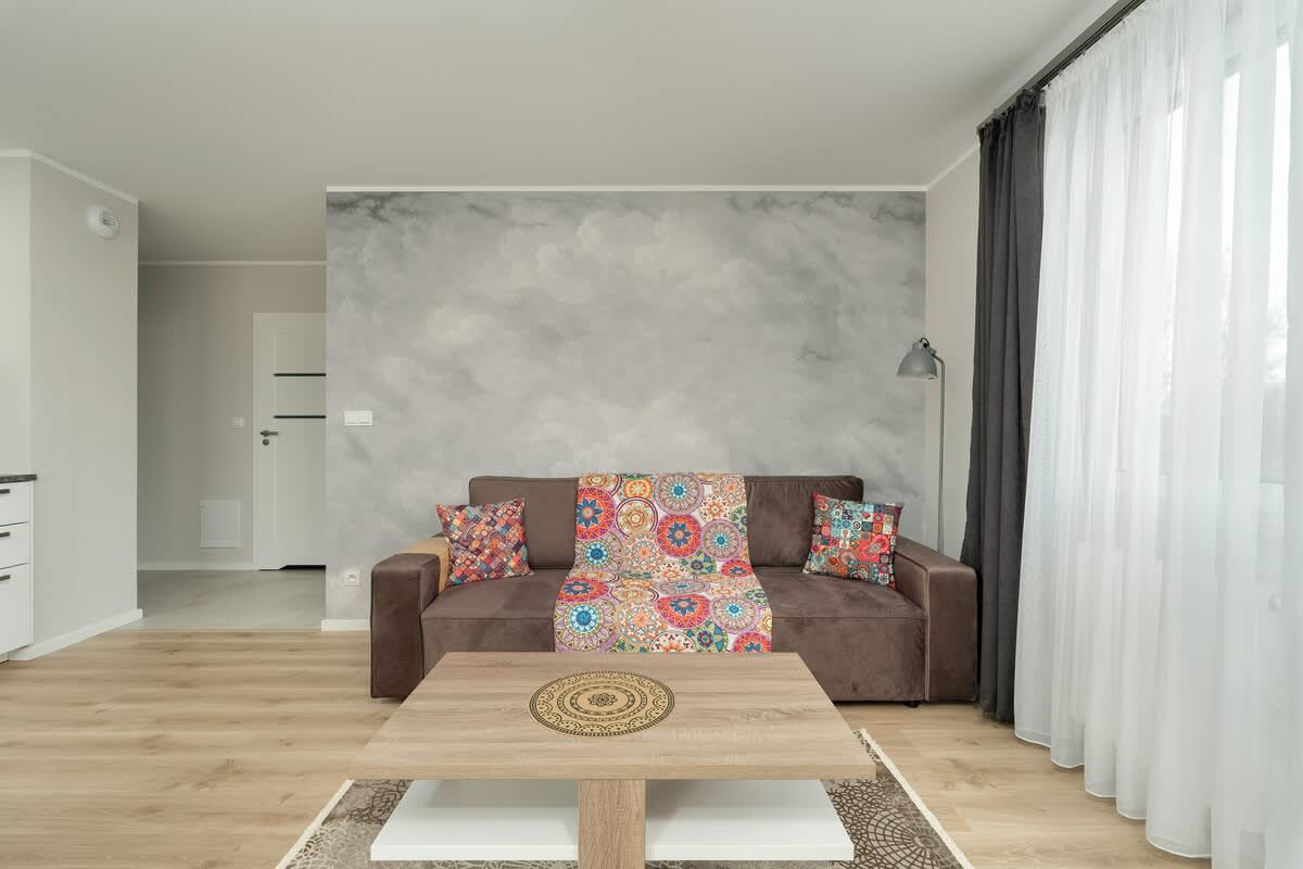 Another view of the living room and dining area. A round table with white chairs is placed in front of large windows, and a sofa is visible to the left. The overall look is light and airy.