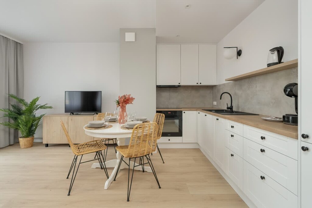 A spacious open-plan kitchen and dining area with white cabinets, wooden countertops, and a chic round dining table with wicker chairs.

