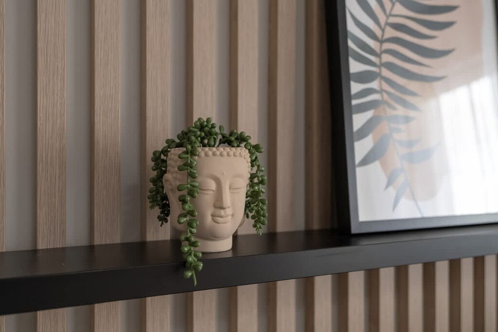 A close-up of a decorative shelf against a wooden panel wall, adorned with a vase and modern botanical artwork.

