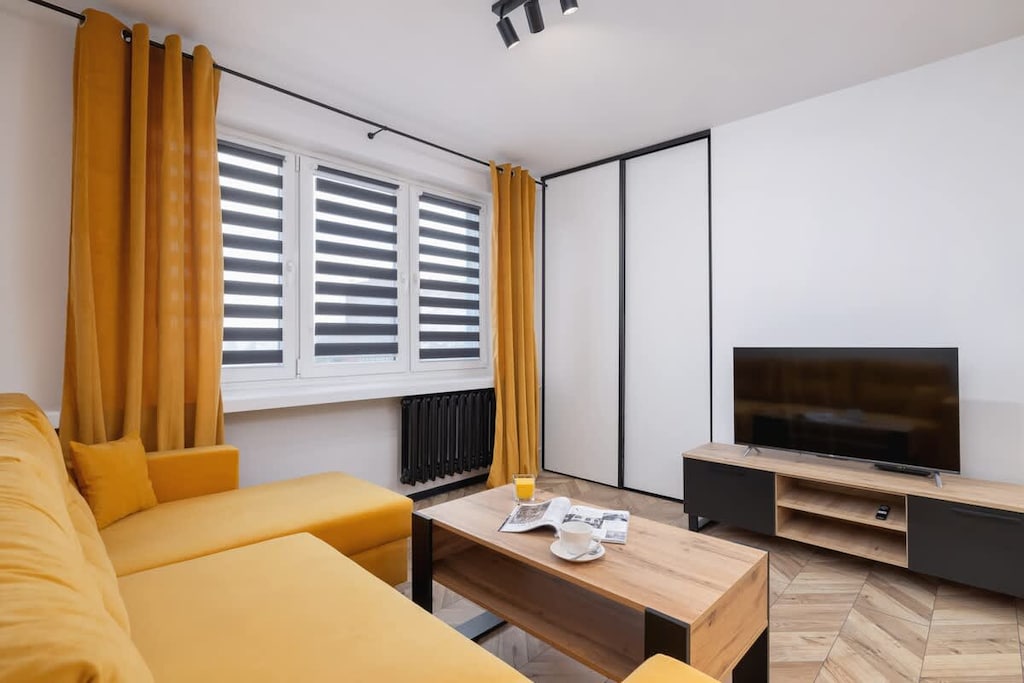 Another angle of the living space, showcasing the yellow sofa, black TV stand, and warm wooden details, creating a welcoming atmosphere.
