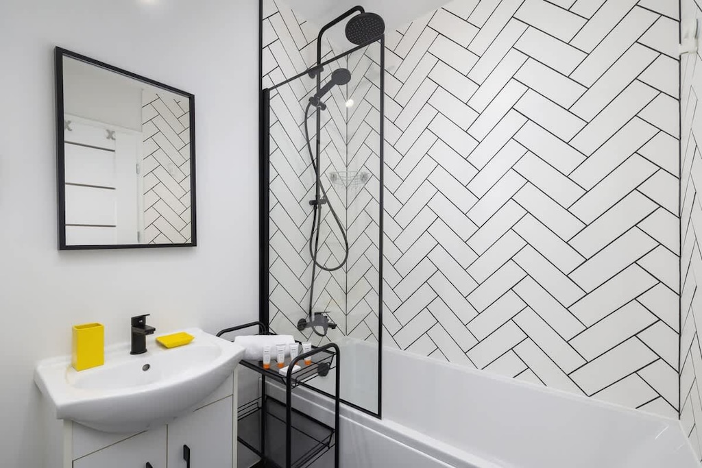 A minimalist bathroom with a white sink, black fixtures, and a stylish herringbone tile pattern on the wall, offering a contemporary design.
