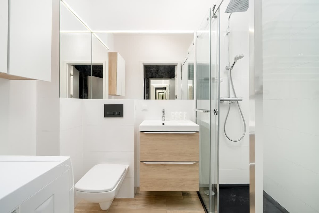 A modern bathroom with a glass-enclosed shower, a wooden vanity, and minimalist fixtures in a neutral color scheme.

