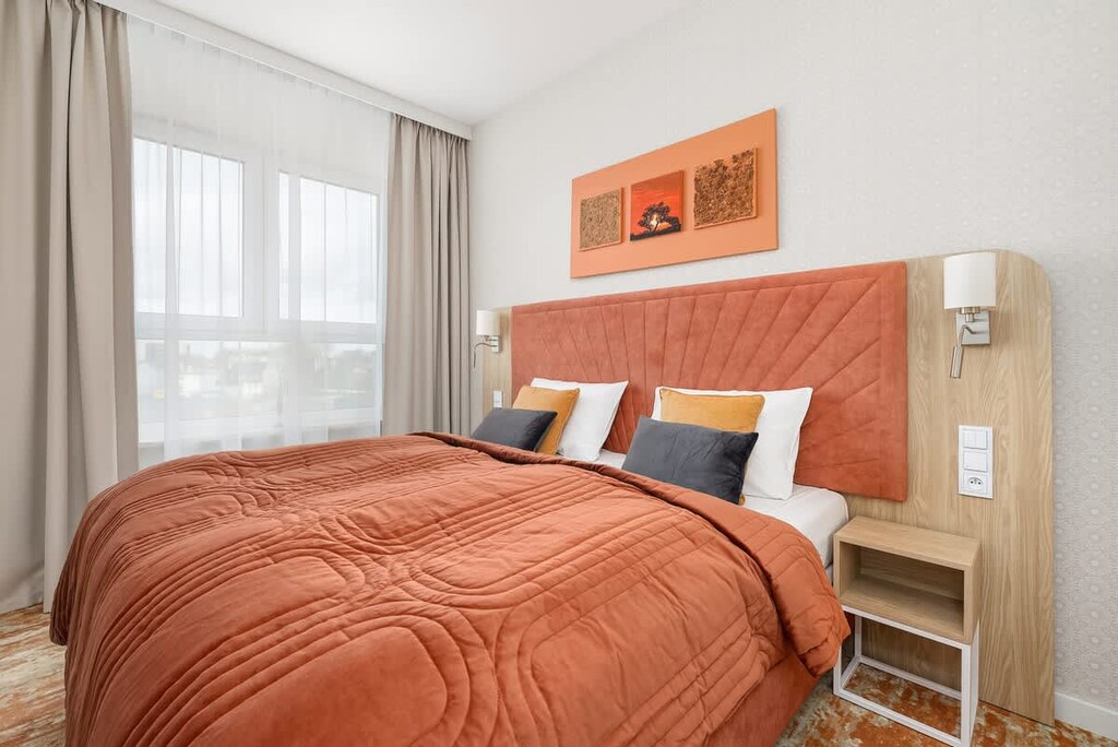 A warmly decorated bedroom with a burnt-orange bedspread, bedside tables with lamps, and framed artwork above the headboard.
