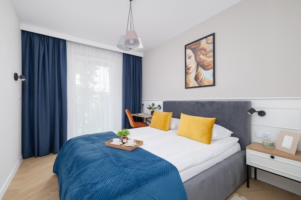 A cozy bedroom with a bed, a desk in the corner, and soft lighting from a window with navy curtains.