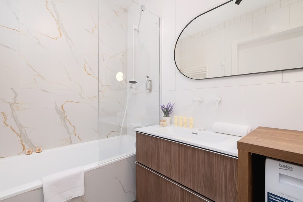 A bathroom with a white bathtub, wooden vanity, and marble-style wall tiles creating a clean aesthetic.