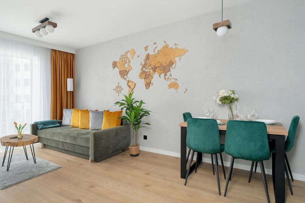 A tastefully furnished living area featuring a sleek wooden dining table, emerald green chairs, and a large world map mural that adds a global, artistic touch to the space.