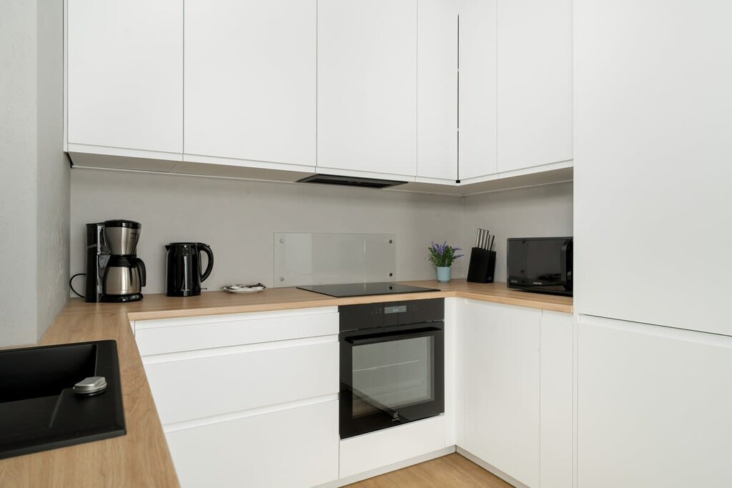 A compact kitchen in pure white tones, equipped with integrated appliances and a clean, uncluttered worktop, emphasizing simplicity and efficiency.