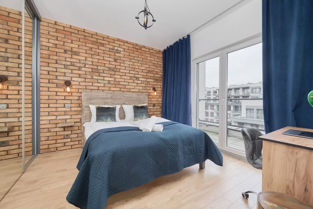A stylish bedroom with a brick accent wall, blue bedding, and navy curtains, creating a cozy ambiance.

