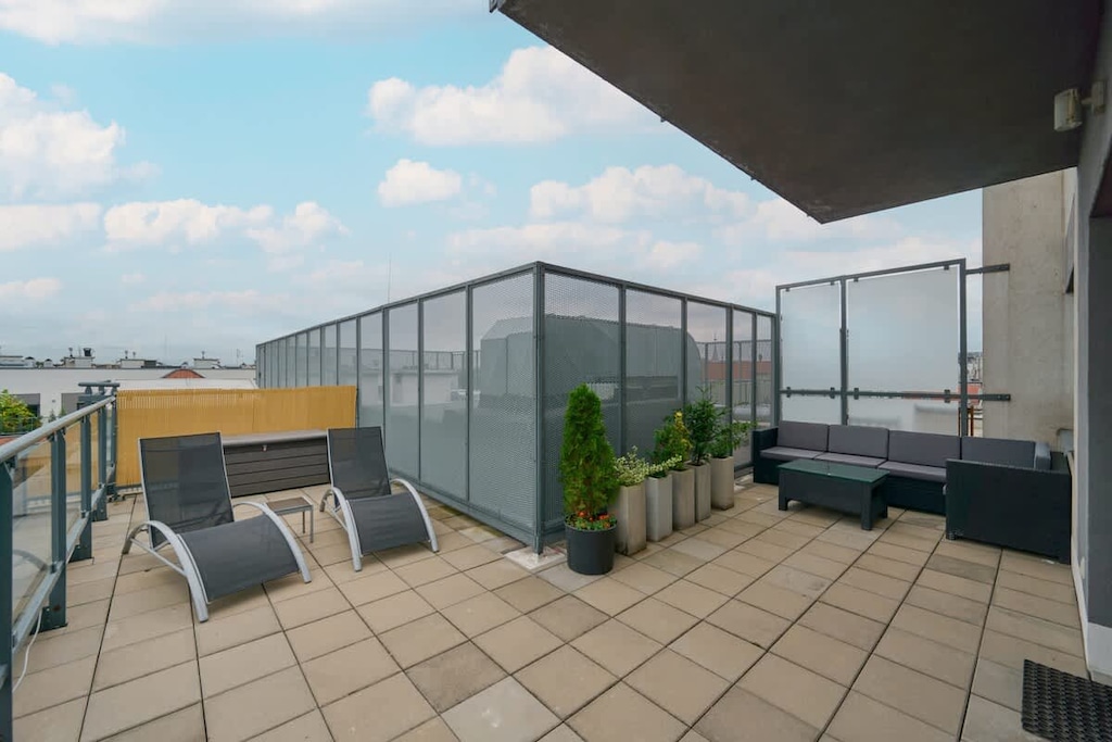 A spacious rooftop terrace with seating areas, potted plants, and panoramic city views.

