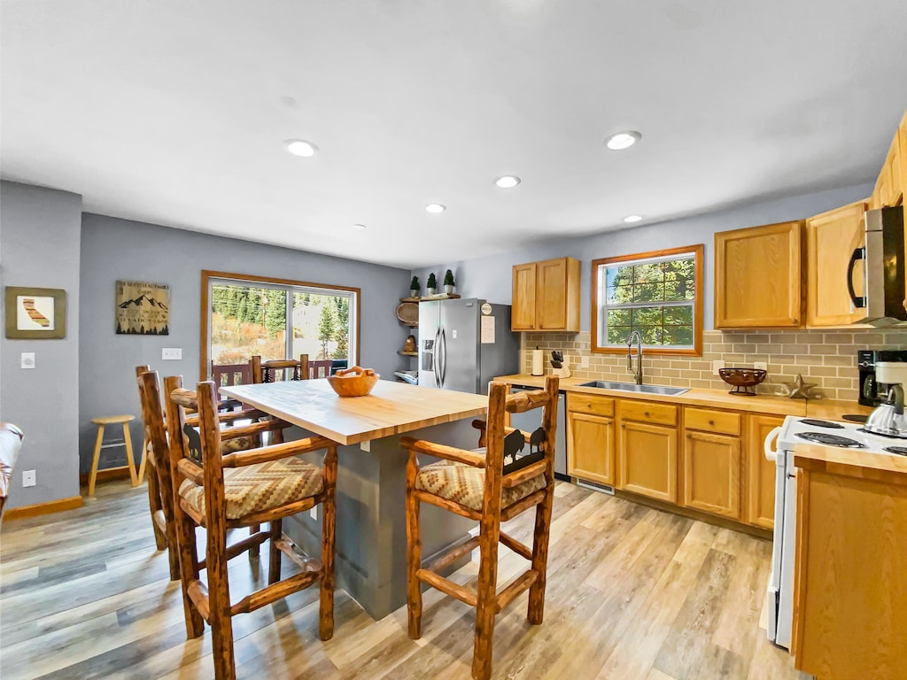 A modern kitchen with wooden cabinetry, a central island with rustic barstools, stainless steel appliances, and large windows providing natural light.