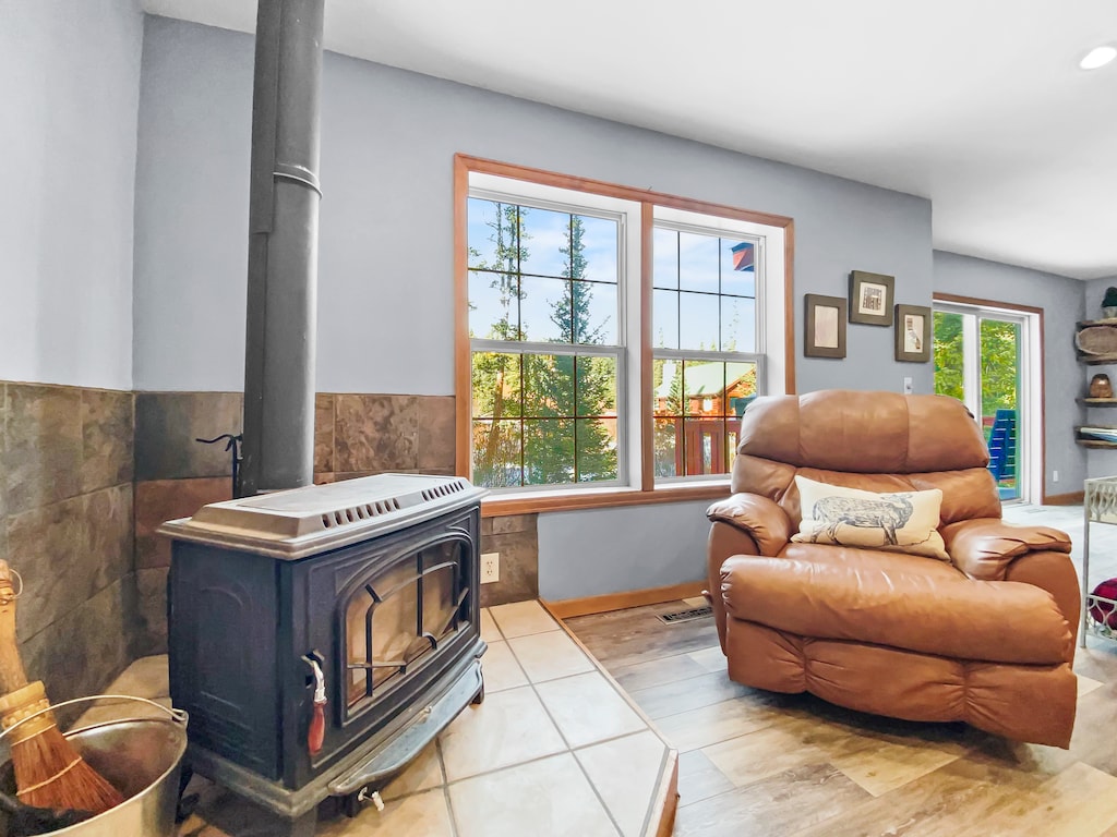 A cozy living area with a wood-burning stove, a leather armchair, and large windows letting in natural light.