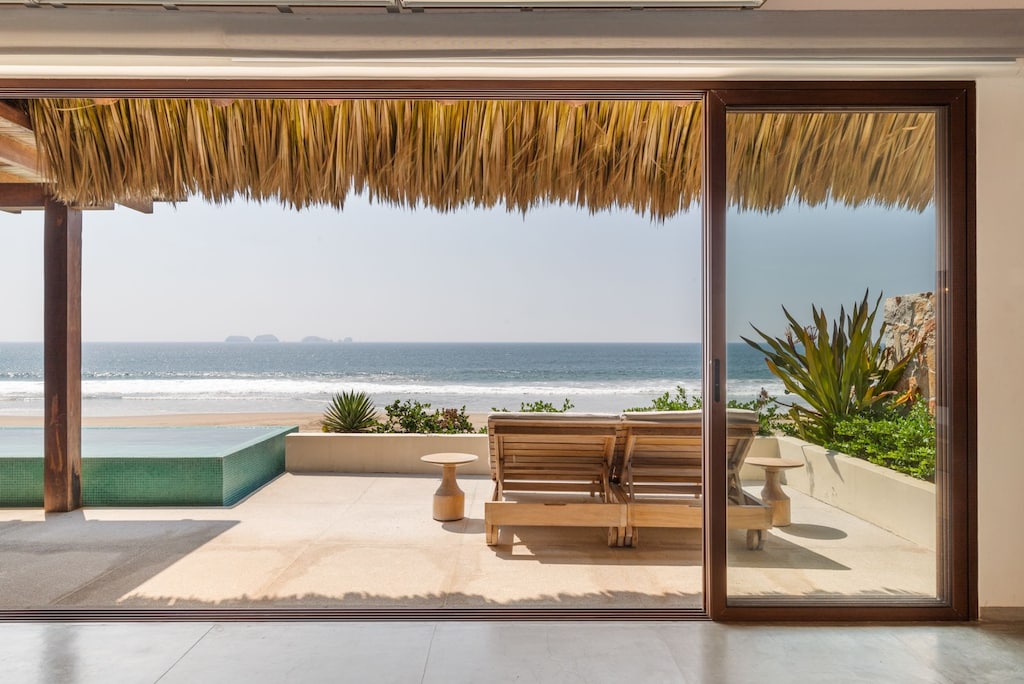 Relax in this stunning beachfront lounge area, featuring a shaded pergola, ocean views, and cozy seating.