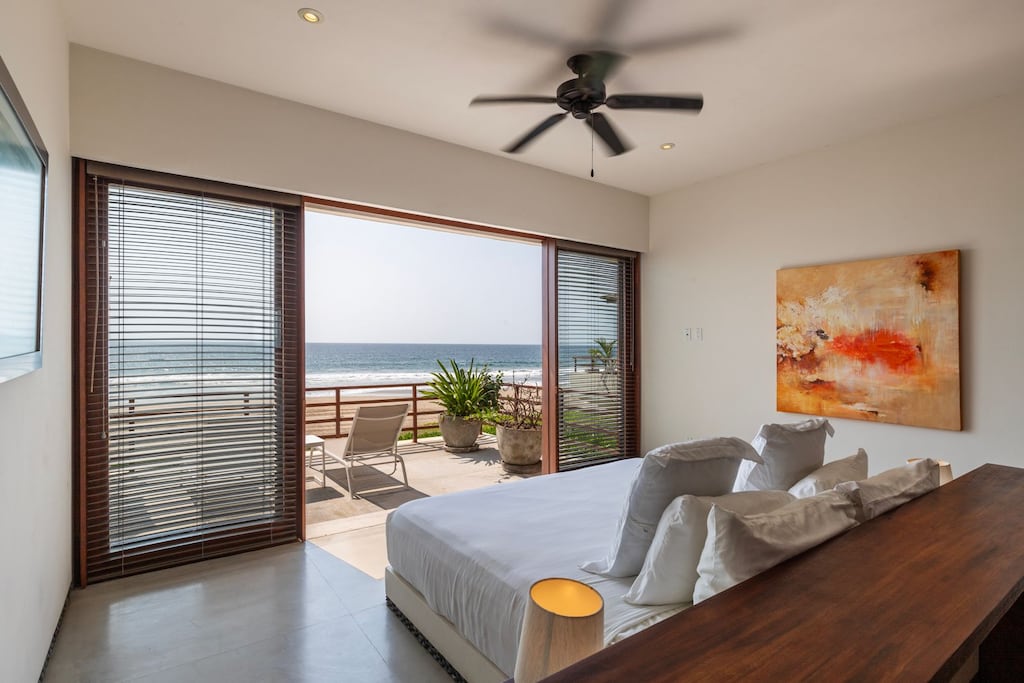 A cozy and elegant bedroom with natural light, warm wooden tones, and direct access to the terrace with ocean views.