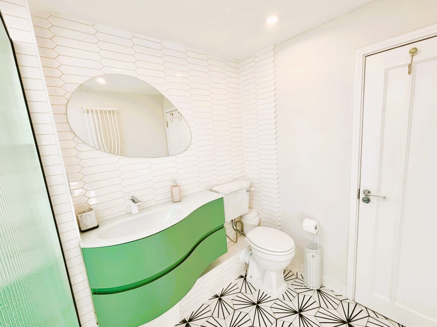 Soft green curves of a modern vanity contrast beautifully with geometric floor tiles and a fluted glass shower screen — a playful yet serene bathroom detail. Soft green curves of a modern vanity contrast beautifully with geometric floor tiles and a fluted glass shower screen — a playful yet serene bathroom detail.