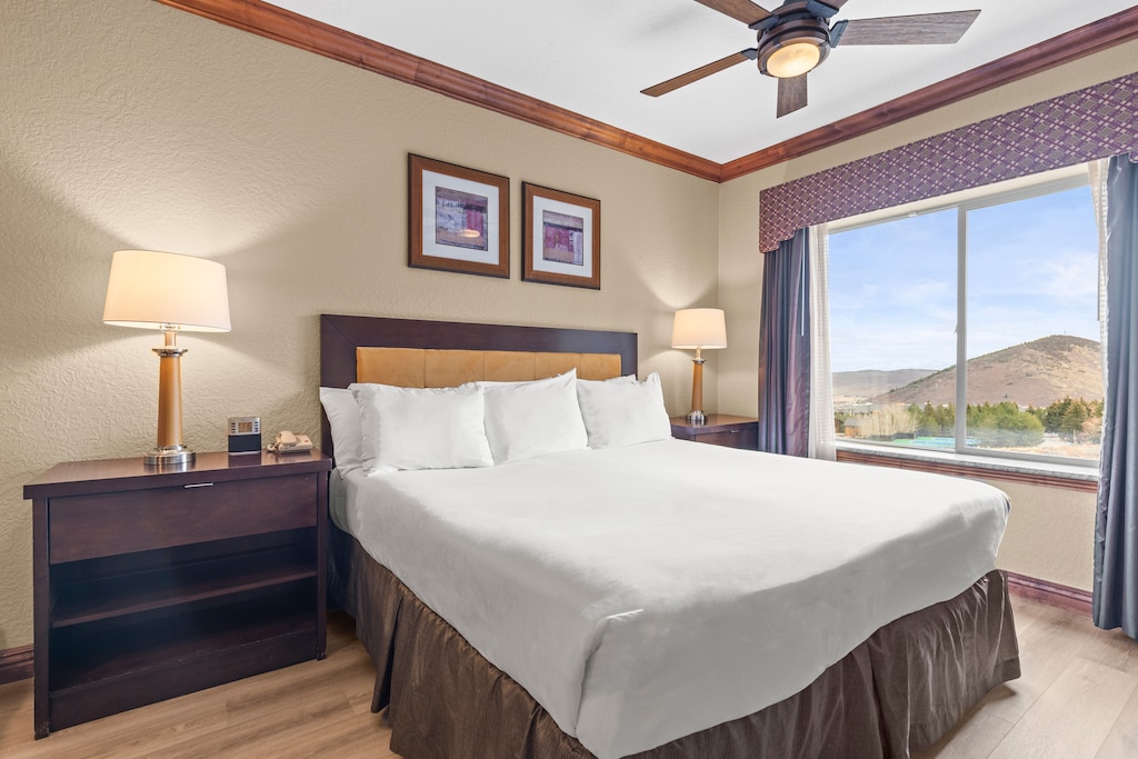 Relax in your comfortable bedroom featuring a plush king bed, ceiling fan for comfort, and a stunning mountain view through large windows.