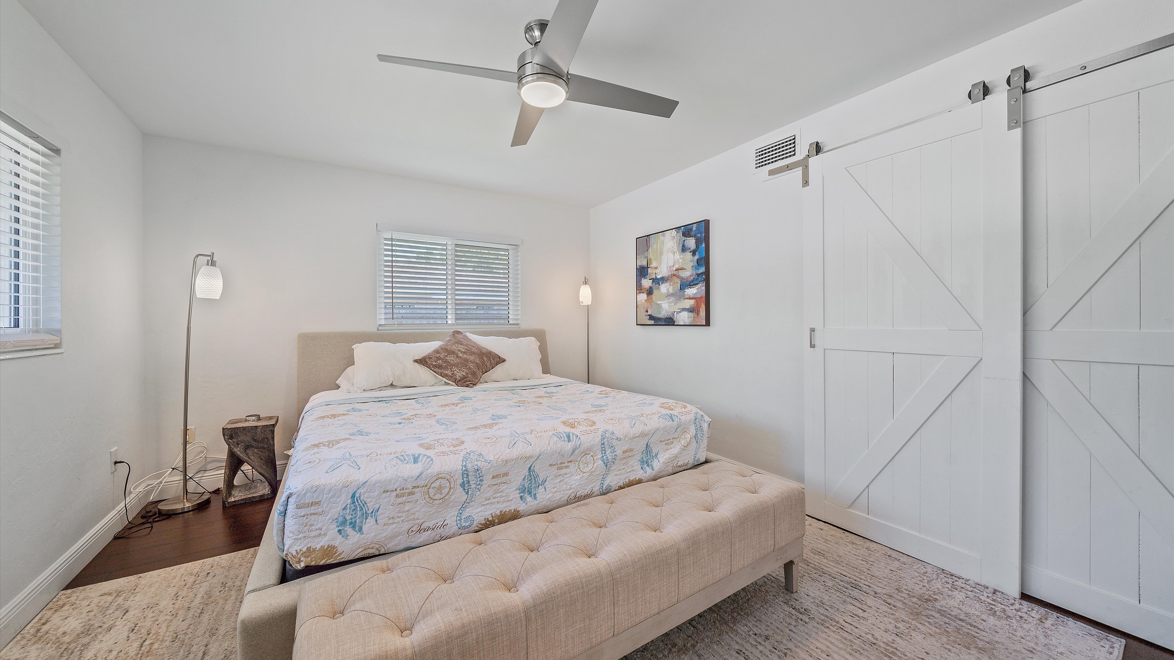 Retreat to the tranquil Primary Suite, featuring a plush King bed, a stylish bench, and contemporary barn doors that perfectly complement the serene coastal decor of this Sarasota home.