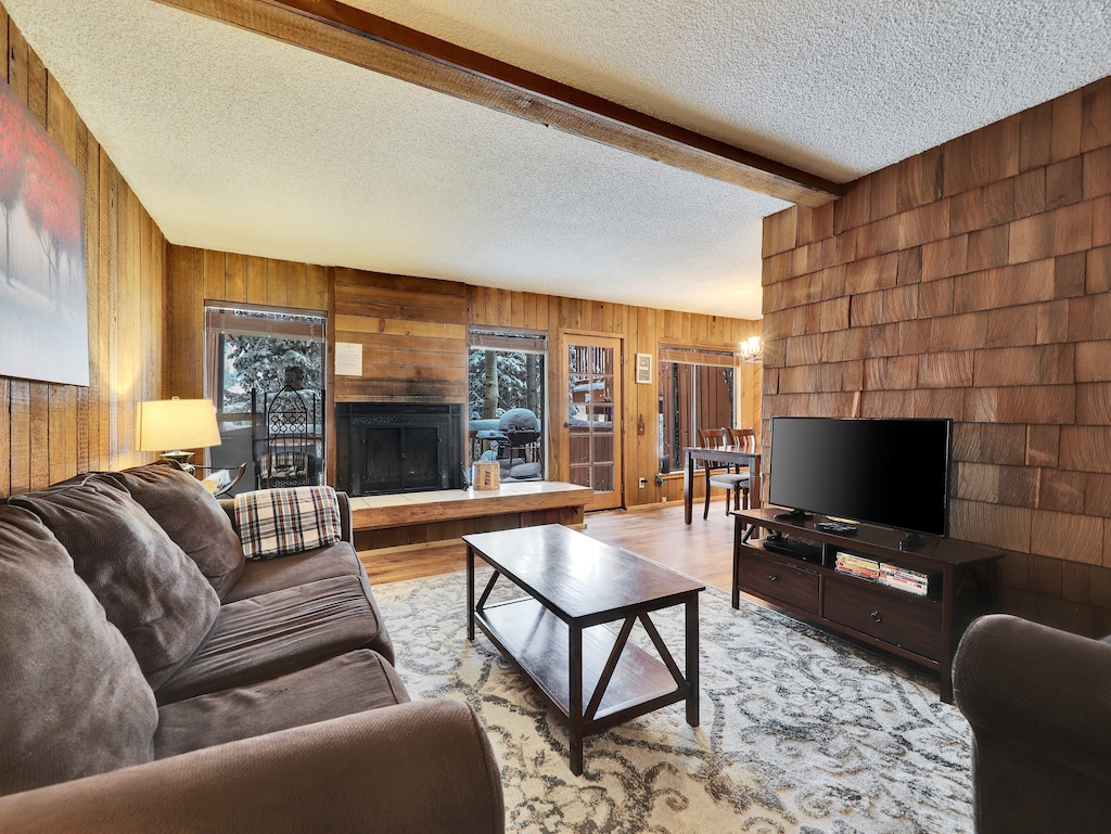 View of the inviting living room featuring comfortable seating, a 55” smart TV, DVD player, and a cozy wood-burning fireplace