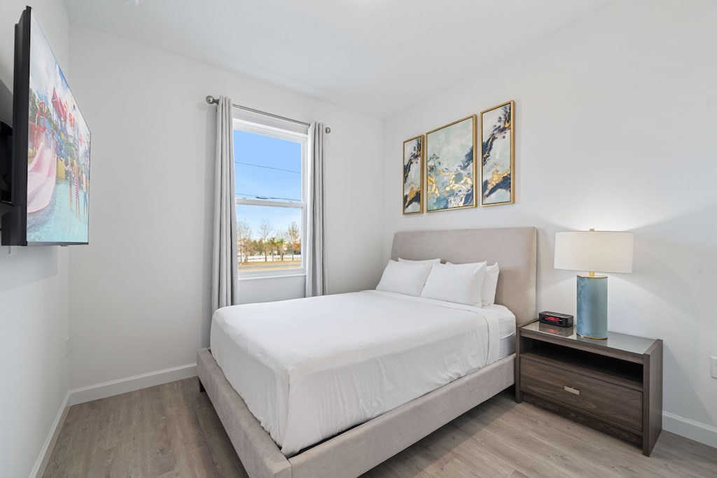 Beautifully designed bedroom featuring a cozy queen bed & modern artwork - Large windows bring in natural light, creating a bright & refreshing atmosphere - Perfect for restful nights & relaxed mornings, complete with a bedside lamp for convenience