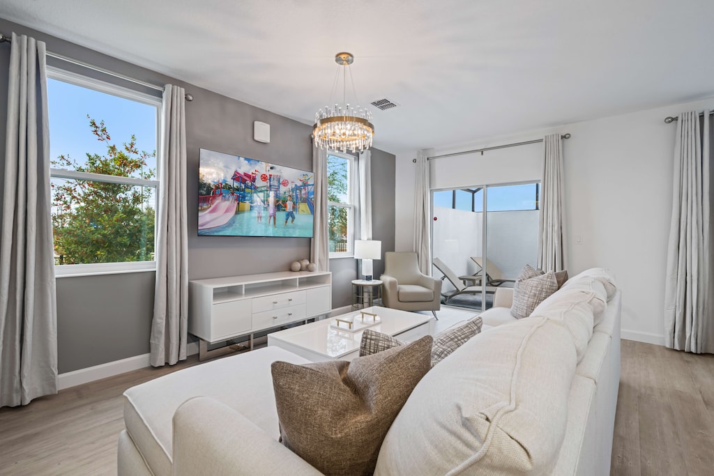 Gather in this bright and stylish living room with comfy seating and elegant decor - Enjoy movie nights on the smart TV or relax under the sparkling chandelier - Large windows fill the space with natural light, creating a welcoming atmosphere