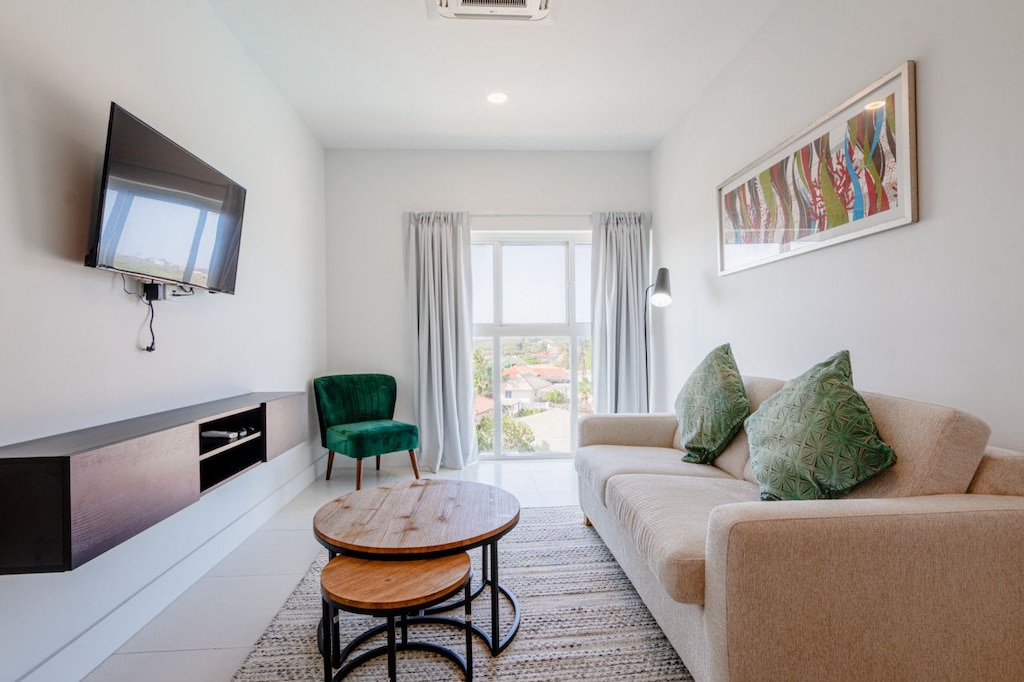 Relax in a bright and welcoming living area with cozy seating and natural light - Enjoy entertainment on a sleek wall mounted smart TV, perfect for unwinding - Stylish decor and serene vibes create an inviting space for ultimate comfort