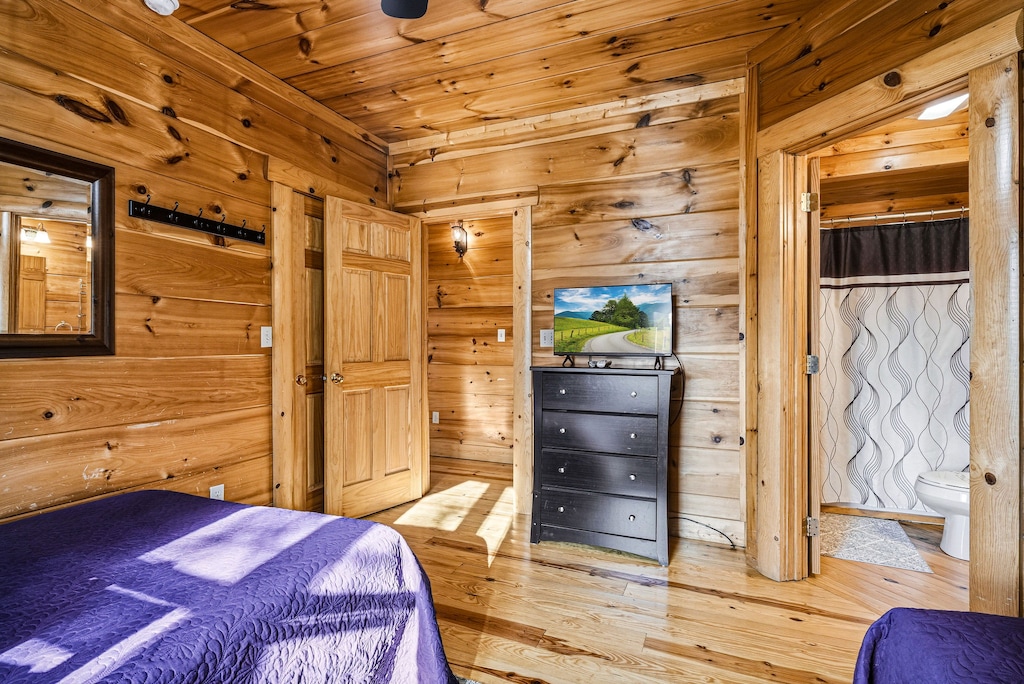 Embrace rustic charm in your wood-paneled bedroom with TV entertainment, private bathroom access, and natural light filtering through windows.