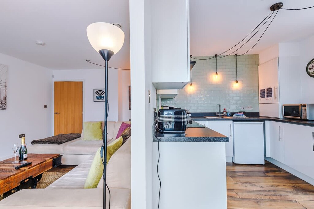 Modern kitchen with white cabinets, dark countertops, and light green subway tiles. Features pendant lighting, coffee maker, kettle, and microwave. A wooden floors add warmth, creating a bright, stylish space for cooking and dining.