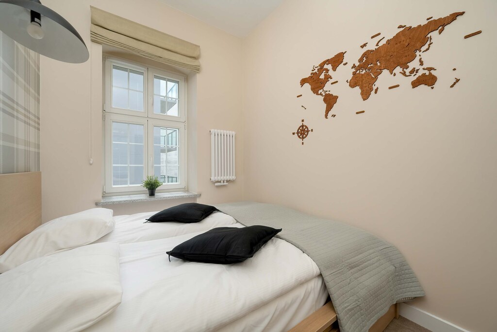 A softly lit bedroom with a double bed, neutral decor, and a wall decal of a world map creating a stylish yet calm atmosphere